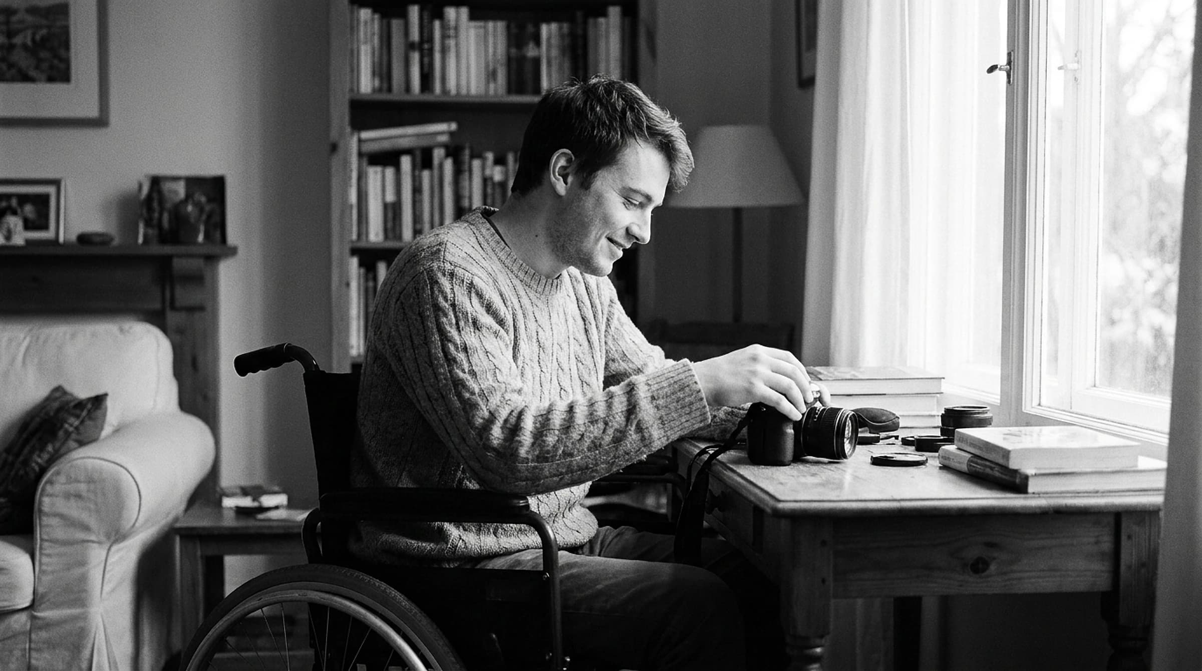 A young man who uses a wheelchair, capable and independent at a desk in a bright, warm home, composed and self-assured
